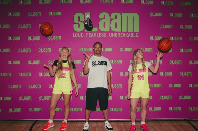 A SLAAM coach with two players in front of the program backdrop.